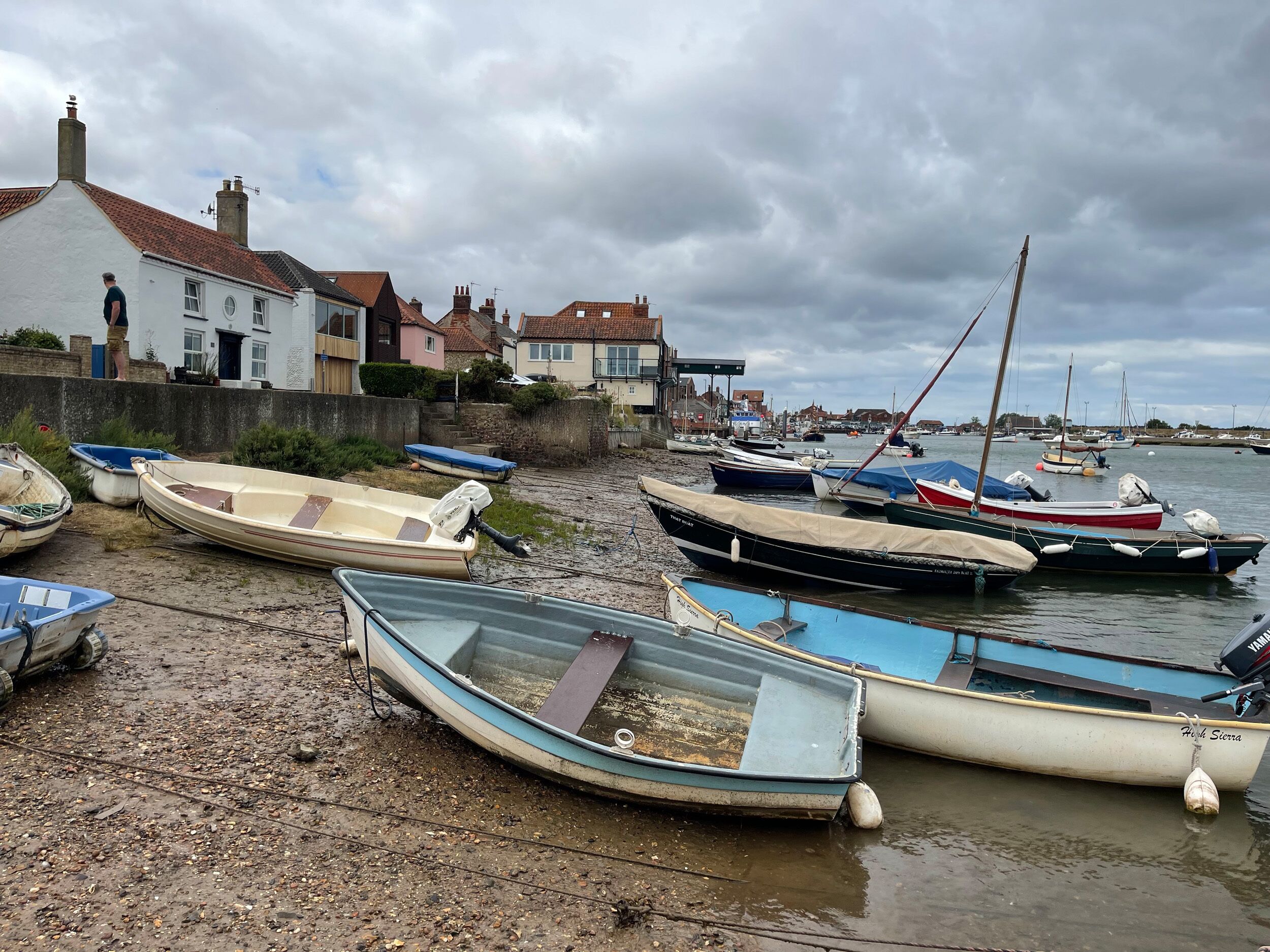 A harbor with boats moored on the shore, a building with a red-tiled roof, and a cloudy sky.