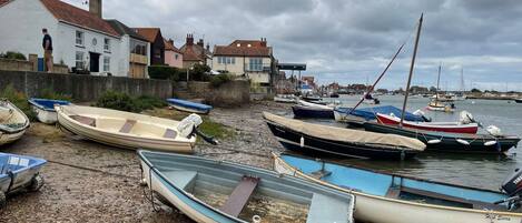 A harbor with boats moored on the shore, a building with a red-tiled roof, and a cloudy sky.