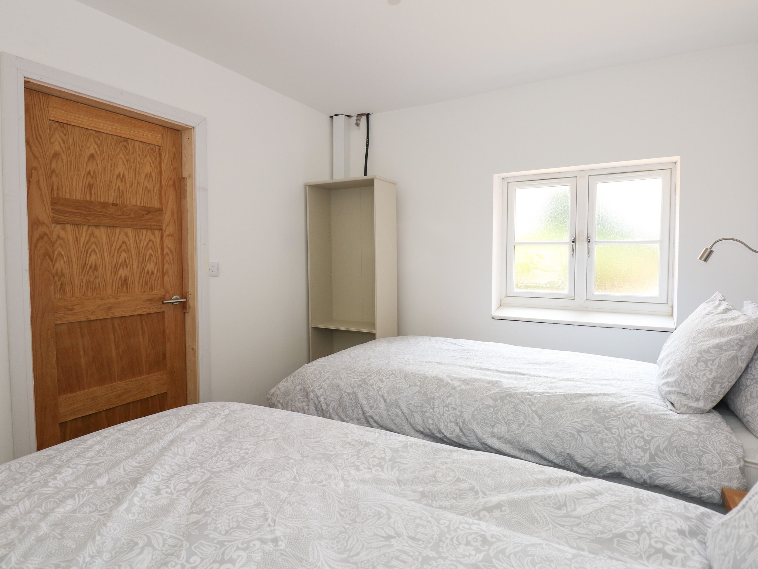 A bedroom with two beds, a wooden door, a window, and a shelf.