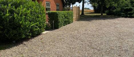 A gravel driveway leading to a brick house with a tiled roof, surrounded by greenery and trees.