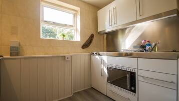 A compact kitchen with a built-in oven, white cabinets, a window, and a wooden wall decoration.