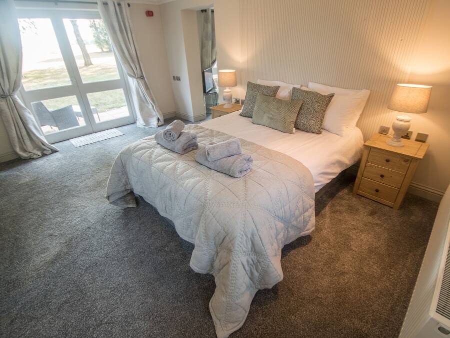 A hotel room with a large bed, a nightstand, a lamp, and a view of the outdoors through a sliding door.