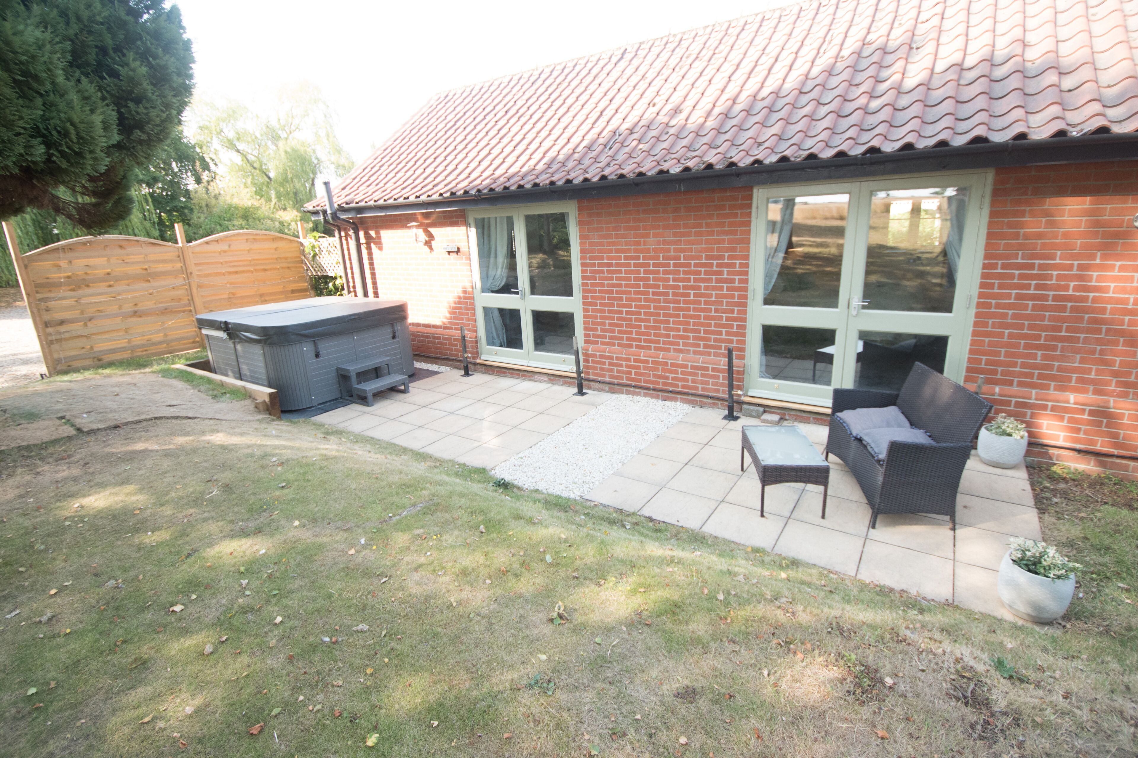 A patio with a barbecue grill, outdoor furniture, and a brick house with a tiled roof.