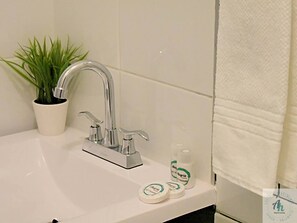 Bathroom features a modern sink with a chrome faucet and a potted plant, along with a towel rack and toiletry items.