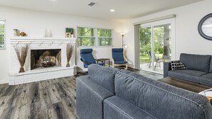 Una sala de estar moderna con chimenea, dos sillas azules, un sofá gris y un ventanal con vistas a la vegetación.
