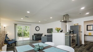Una cocina moderna con horno y refrigerador integrados, un comedor con mesa y sillas, y una sala de estar con sofá y televisor.