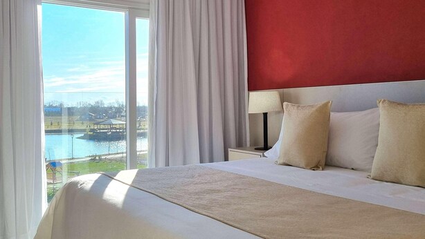Une chambre d’hôtel avec un grand lit, une table de chevet, une lampe et une vue sur un plan d’eau et des bâtiments.
