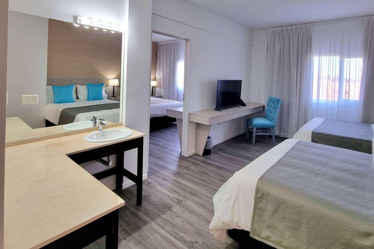 Hotellihuone, jossa on kaksi sänkyä, työpöytä, jossa on televisio, kylpyhuone, jossa on pesuallas, ja peili.