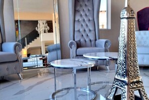 Moderni sisustus, jossa on lasinen Eiffel-tornin pienoismalli, kaksi pyöreää pöytää ja napitettu sohva.