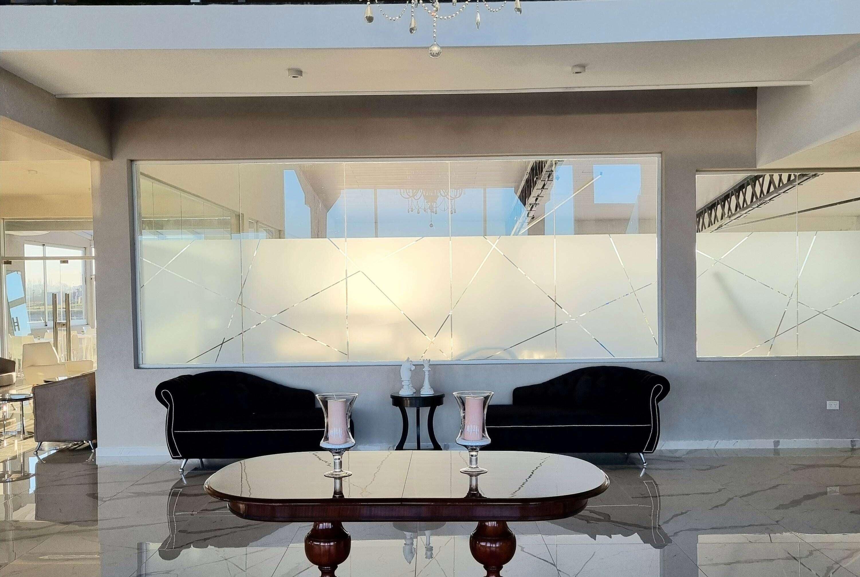 Un interior moderno con un suelo de mármol reflectante, una mesa redonda con dos jarrones y dos sofás negros.