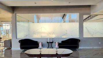 Un interior moderno con un suelo de mármol reflectante, una mesa redonda con dos jarrones y dos sofás negros.