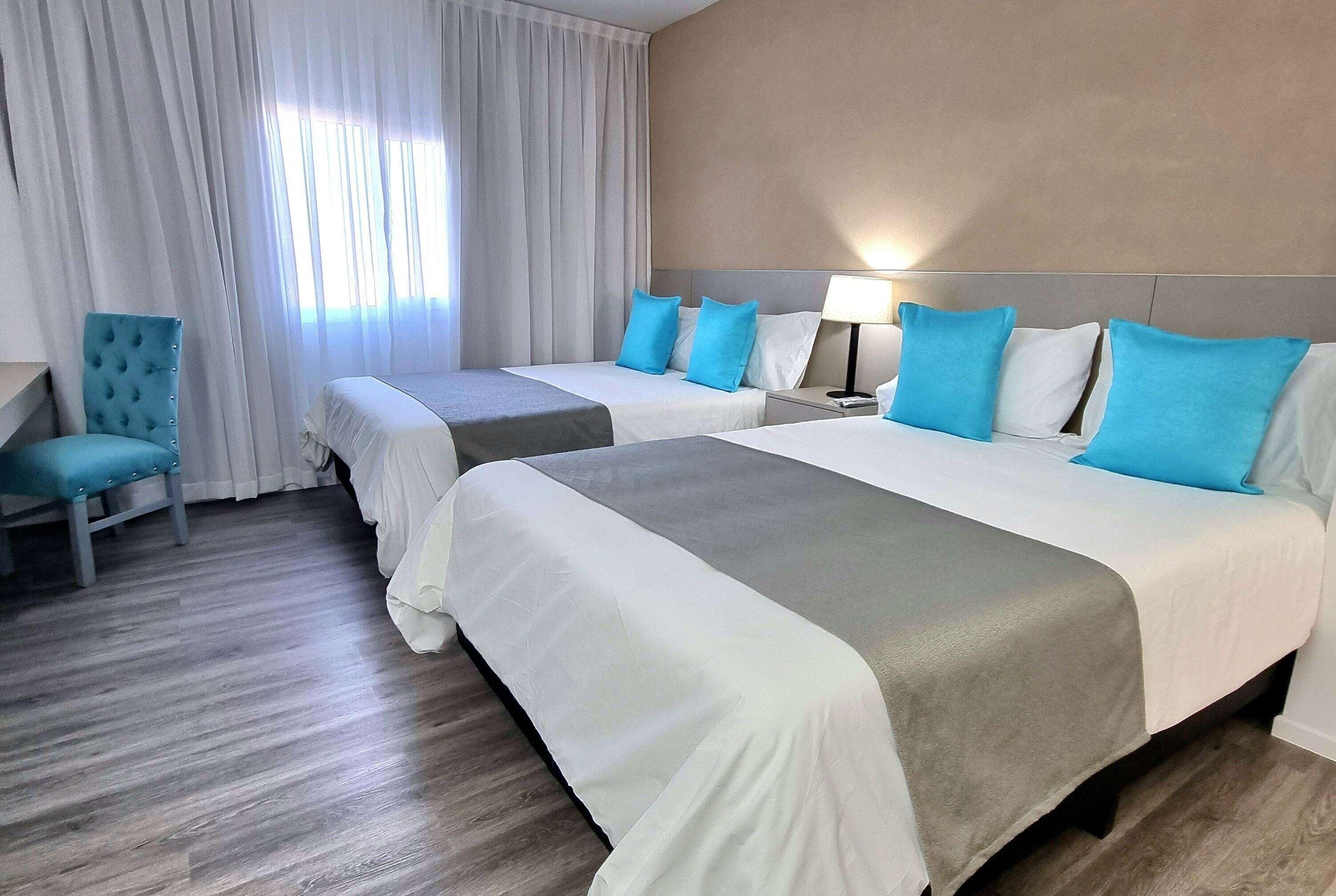 A hotel room with two beds, a chair, a nightstand, and a lamp.