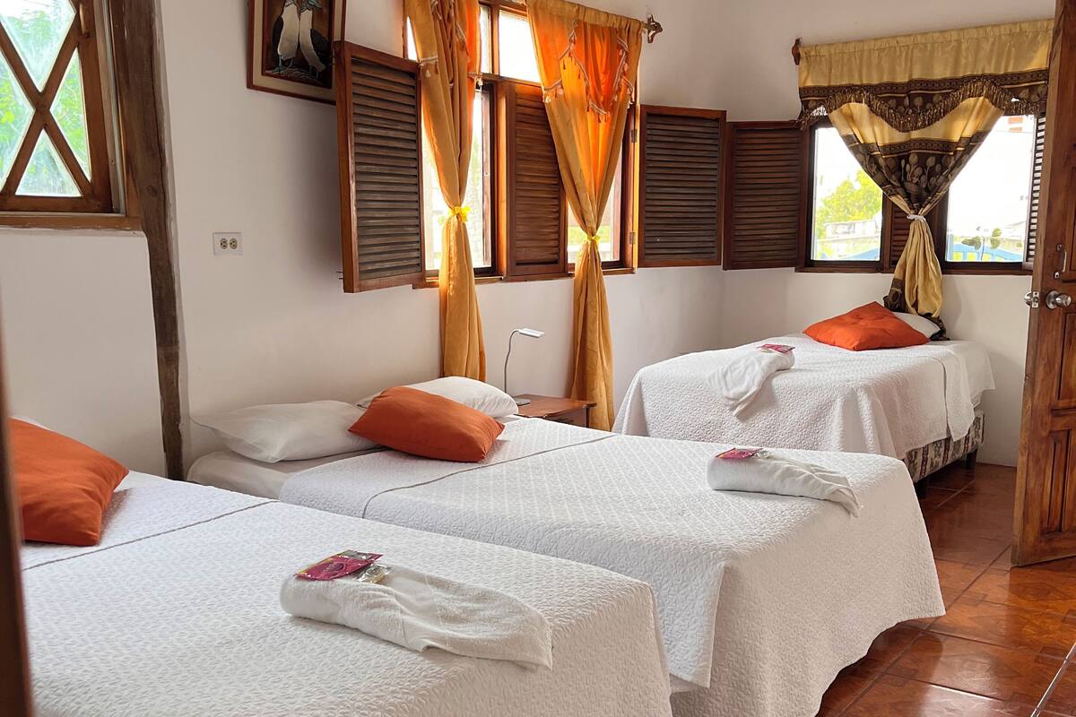 A hotel room with two beds, a window with curtains, an air conditioning unit, and a tiled floor.