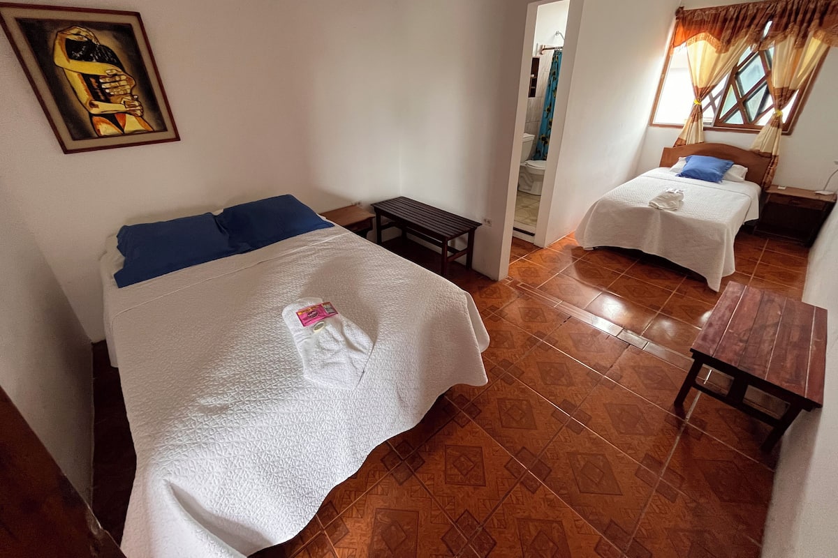 A hotel room with two beds, a small table, a bench, and a painting on the wall.