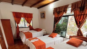 Une chambre avec quatre lits disposés en rangée, chacun étant agrémenté de draps blancs et de touches de couleur orange.