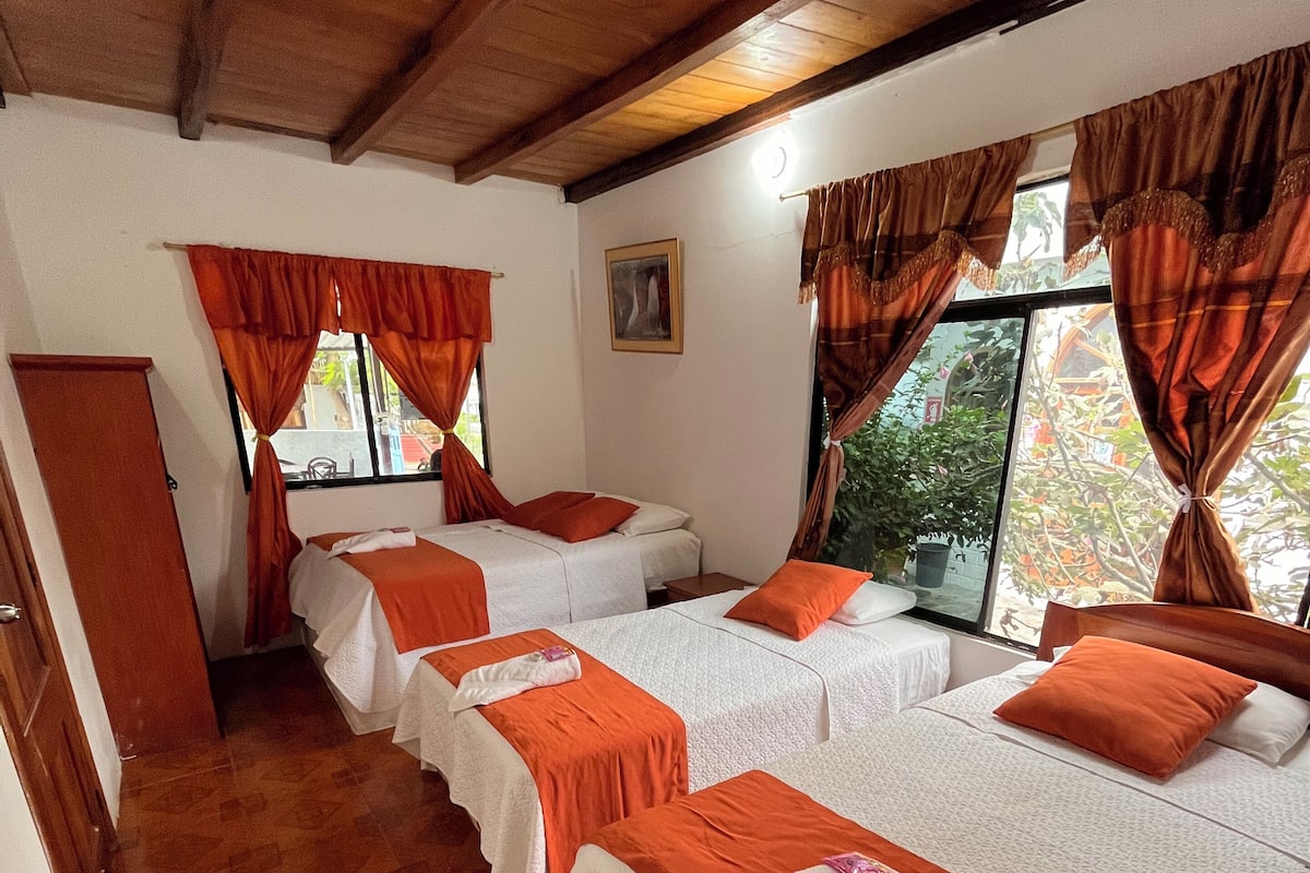 A room with four beds arranged in a row, each with white bedding and orange accents.