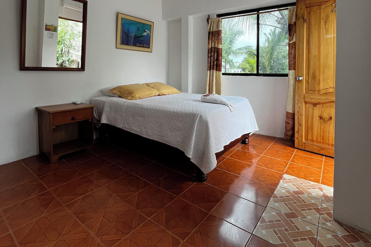 A bedroom with a bed, a nightstand, a window with curtains, and a wooden door.