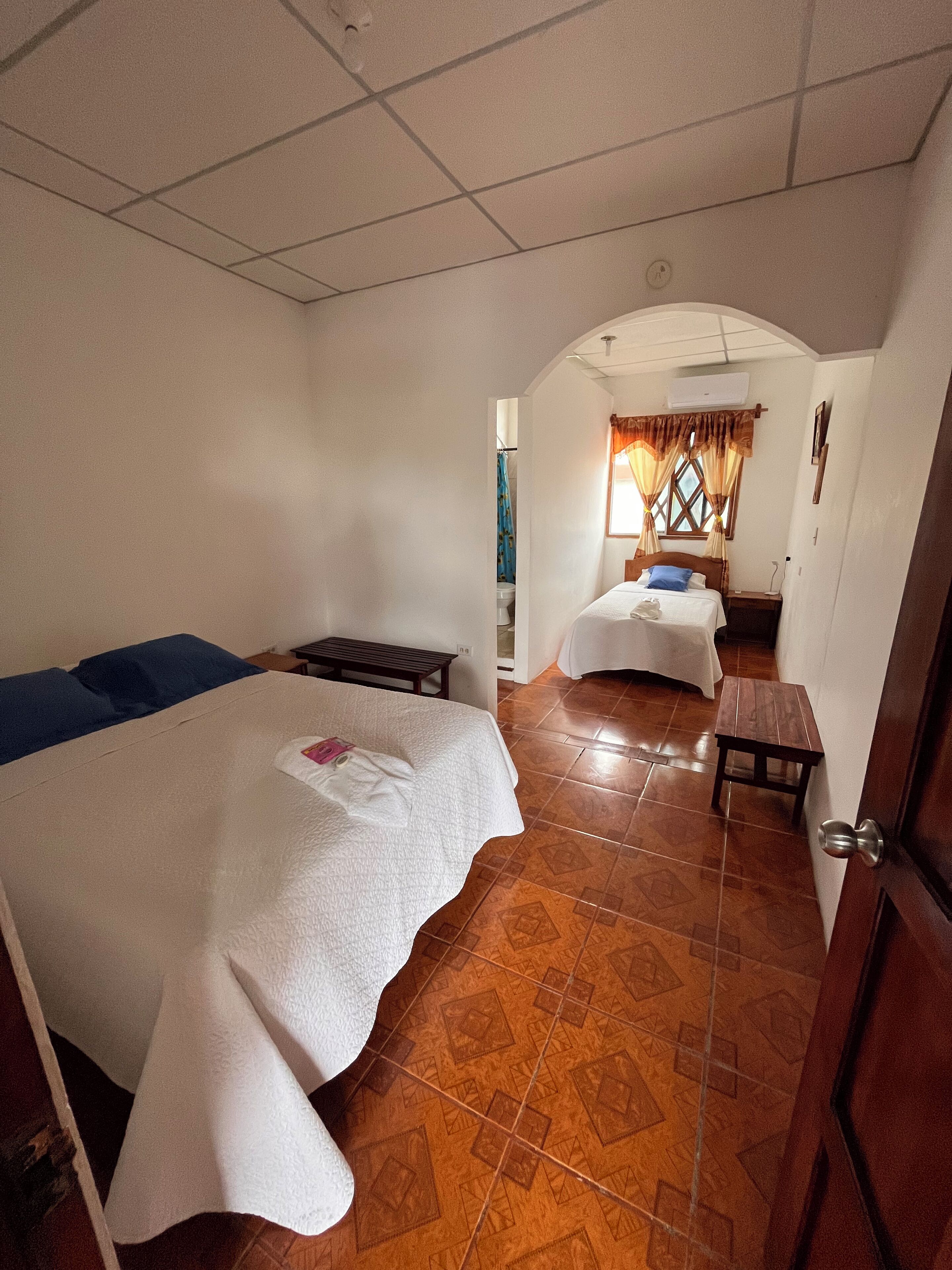 Habitación de hotel con dos camas, una mesita y un baño visible a través de un arco.