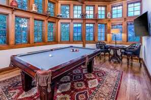 A pool table in a room with large windows, a fireplace, and a television.