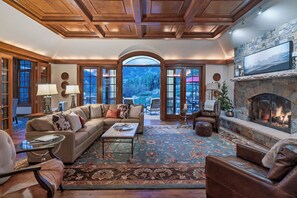A spacious living room with a fireplace, comfortable seating, and a view of a mountainous landscape through large windows.