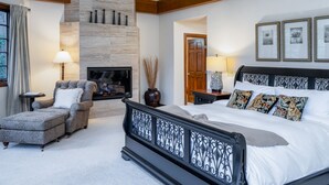 Une chambre à coucher avec une cheminée, un grand lit, une chaise et une table de chevet.