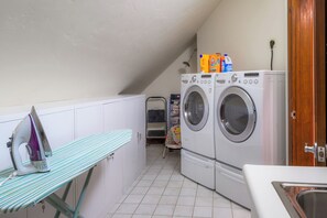 Un cuarto de lavandería con lavadora, secadora, tabla de planchar y soporte.