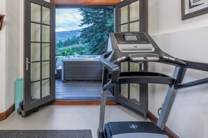 A treadmill in a room with a large window leading to a deck with a hot tub.