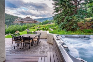 Un patio exterior con un jacuzzi, una mesa con sillas y vistas a un paisaje montañoso.
