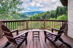 A wooden deck with two Adirondack chairs and a small table, overlooking a mountainous landscape.