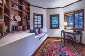 A cozy reading nook with a built-in bench, a wooden bookshelf, and a desk with a lamp.