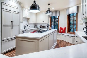 A modern kitchen with white cabinetry, a central island, and a window with a view of trees.