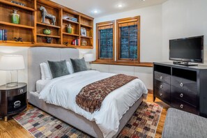 A bedroom with a bed, bedside tables, a TV, a dresser, and a window with a view.