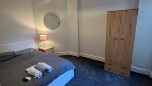 Un dormitorio con una cama, una lámpara de noche, un armario de madera y un reloj de pared.