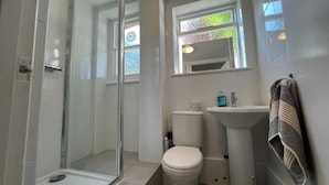 Un baño con ducha de vidrio, inodoro, lavamanos y ventana con vistas.