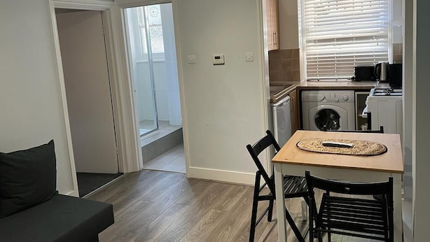 Un espacio habitable compacto con kitchenette, una zona de comedor con mesa y sillas, y un sofá.