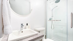 A modern bathroom with a white sink, mirror, toilet, and glass-enclosed shower. - Bright Modern Loft | Walk Everywhere, (1405) Lumineux loft (Québec City)