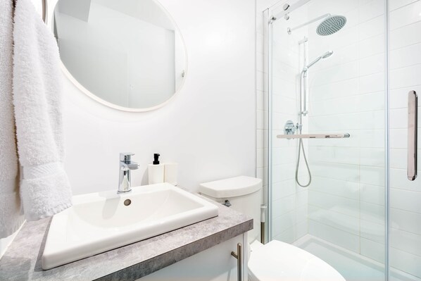 A modern bathroom with a white sink, mirror, toilet, and glass-enclosed shower.