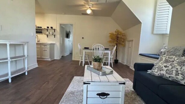 A spacious living area with a dark wood floor, a white sofa with patterned cushions, a white coffee table with a tray, and a dining area with white chairs and a small plant. - Sunsets & Shows! Gorgeous, Private 1 BR Listing! (Mesa)