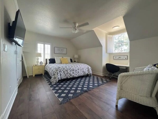 Een slaapkamer met een bed, een bureau, een stoel, een plafondventilator en een raam.