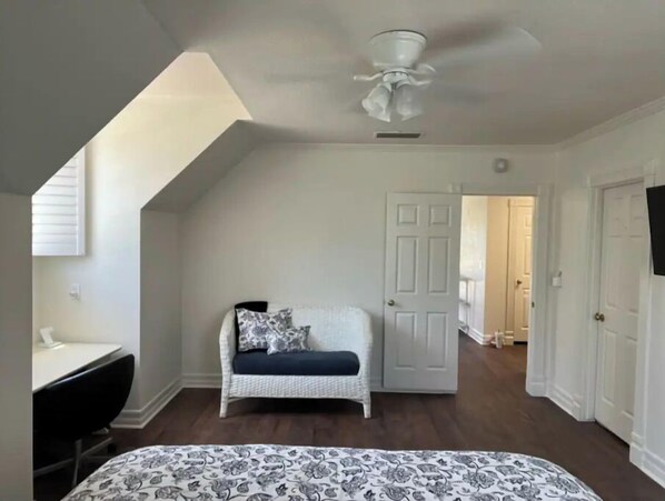A bedroom with a bed, a desk, a chair, a white door, and a ceiling fan.