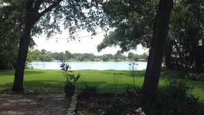 Un sendero en un jardín que lleva a un lago, rodeado de árboles y plantas en macetas.