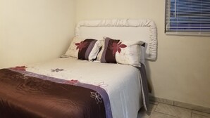 Ein Schlafzimmer mit Bett, Kissen, einem Fenster mit Jalousien und einer Klimaanlage an der Wand.