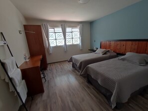 Una habitación con dos camas, un escritorio de madera, una silla y una ventana con cortinas.
