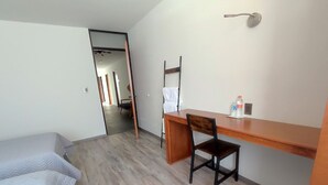 A small, neatly arranged room with a bed, a desk, and a chair. There is a door leading to another room. - El salto de Camela (Uruapan)