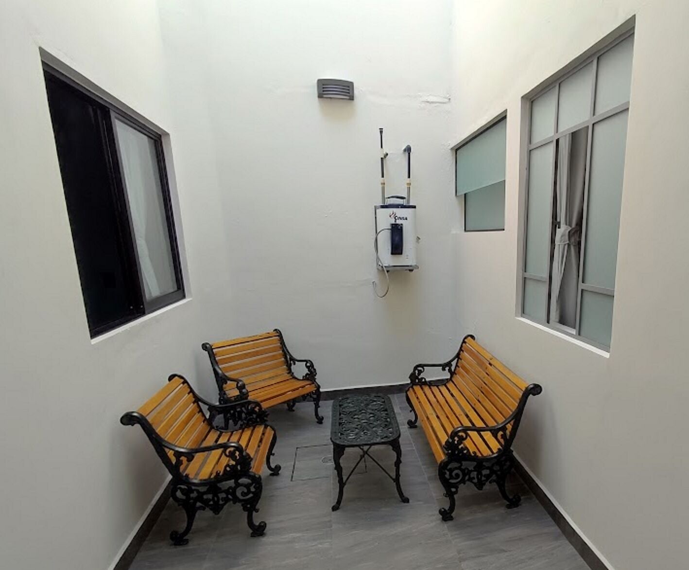 A small, enclosed patio area with two wooden benches and a table, white walls, and a window on one side.