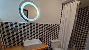 A bathroom with a geometric patterned wall, a round mirror, a white sink, and a toilet. - El salto de Camela (Uruapan)