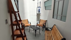 A narrow corridor with wooden benches and a table, a water dispenser, and a window with blinds. - El salto de Camela (Uruapan)