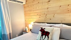 Une chambre avec une tête de lit en bois, un lit avec une literie à rayures, un coussin à l’effigie d’un élan et une table de chevet avec une lampe.