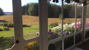 A covered porch with a view of a landscaped garden and a field. - Classic, on the water stunner! Owner occupied with full amenities! (Saint George)