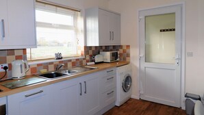 A compact kitchen with white cabinets, a built-in microwave, a sink, and a washing machine. - The Paddocks -  a bungalow situated in a rural village surrounded by fields and horses (Frettenham)
